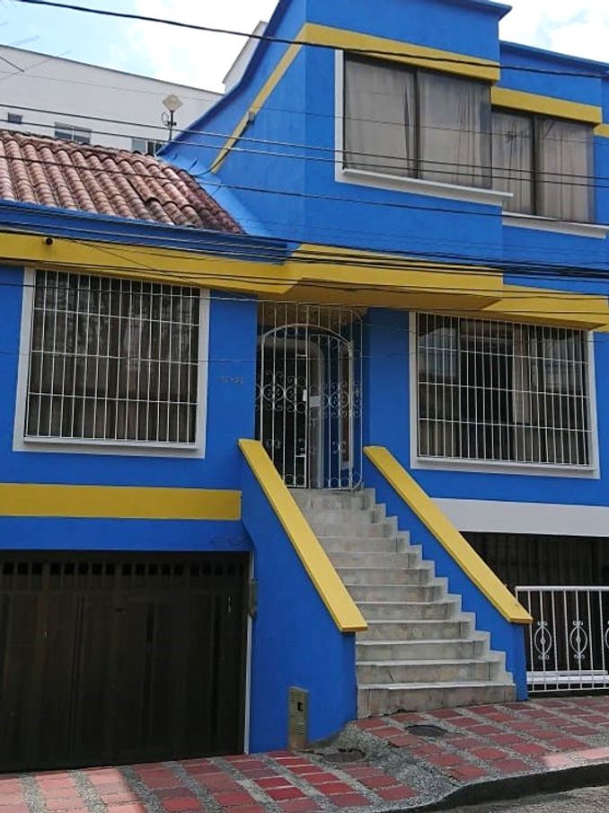 Fachada de Casa Azul: casa azul de dos pisos con franjas amarillas, rejas blancas y escalera con muros amarillos hacia la entrada.