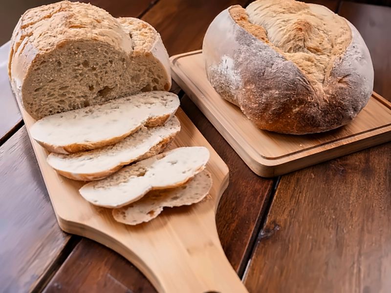 Dos panes de masa madre sobre tablas de madera, uno de ellos tajado, en una mesa del café.