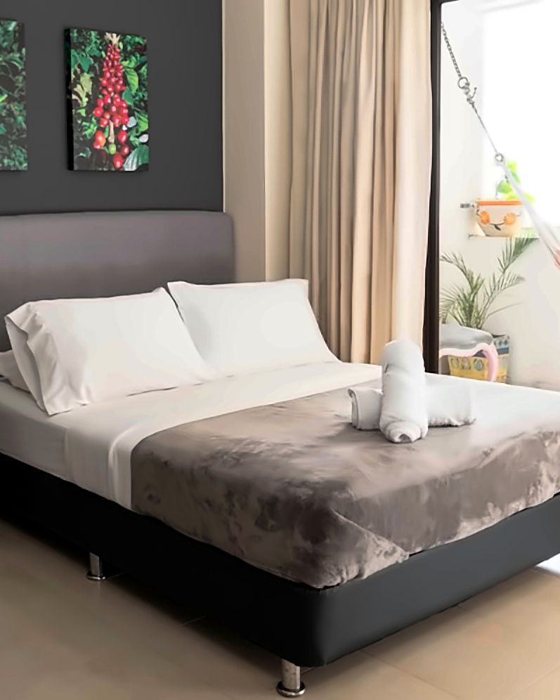 Habitación Castillo: cama doble con cubrelecho gris, pared oscura con cuadros de flor y fruto de café, litera de madera a la izquierda y balcón con hamaca.