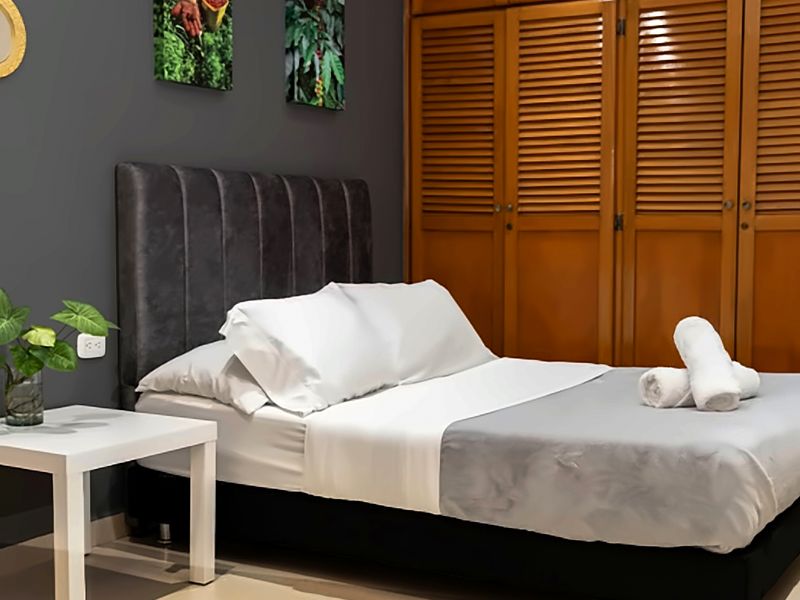 Habitación con cama doble, pared gris con cuadros de café, espejo dorado y clósets de madera con persianas.