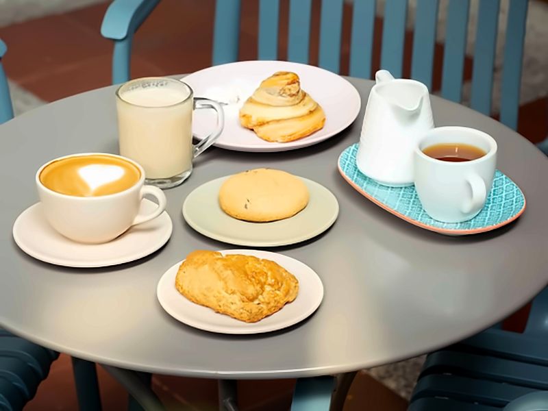 Mesa del patio con un café con arte latte, una bebida con leche, té y tres panes dulces de la casa.