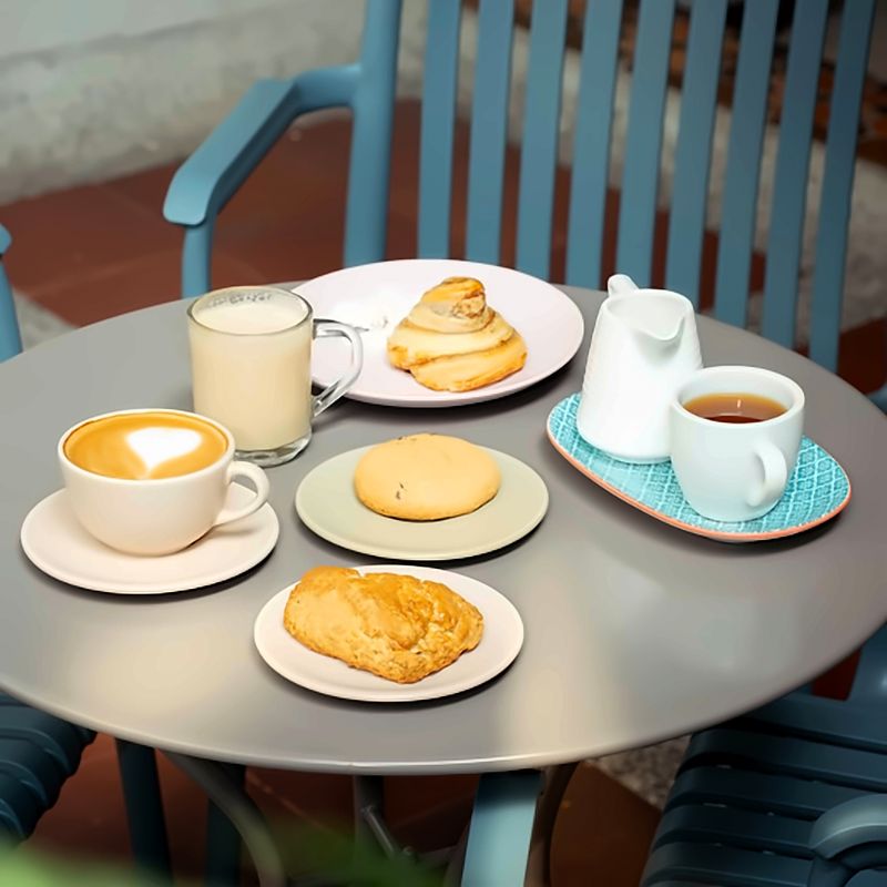 Mesa del patio con un café con arte latte, una bebida con leche, té y tres panes dulces de la casa.