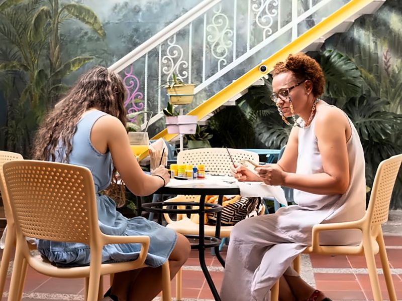 Dos personas pintan en una mesa del patio, frente al mural botánico y la escalera blanca de Casa Azul.