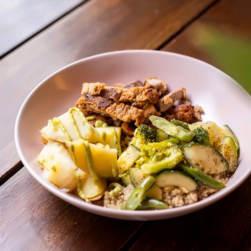 Bowl de quinoa con milanesa, papa y verduras salteadas sobre una mesa de madera.