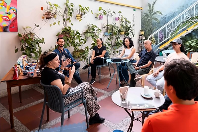 Encuentro en el patio: un grupo grande conversa sentado en círculo entre matas colgantes y el mural.