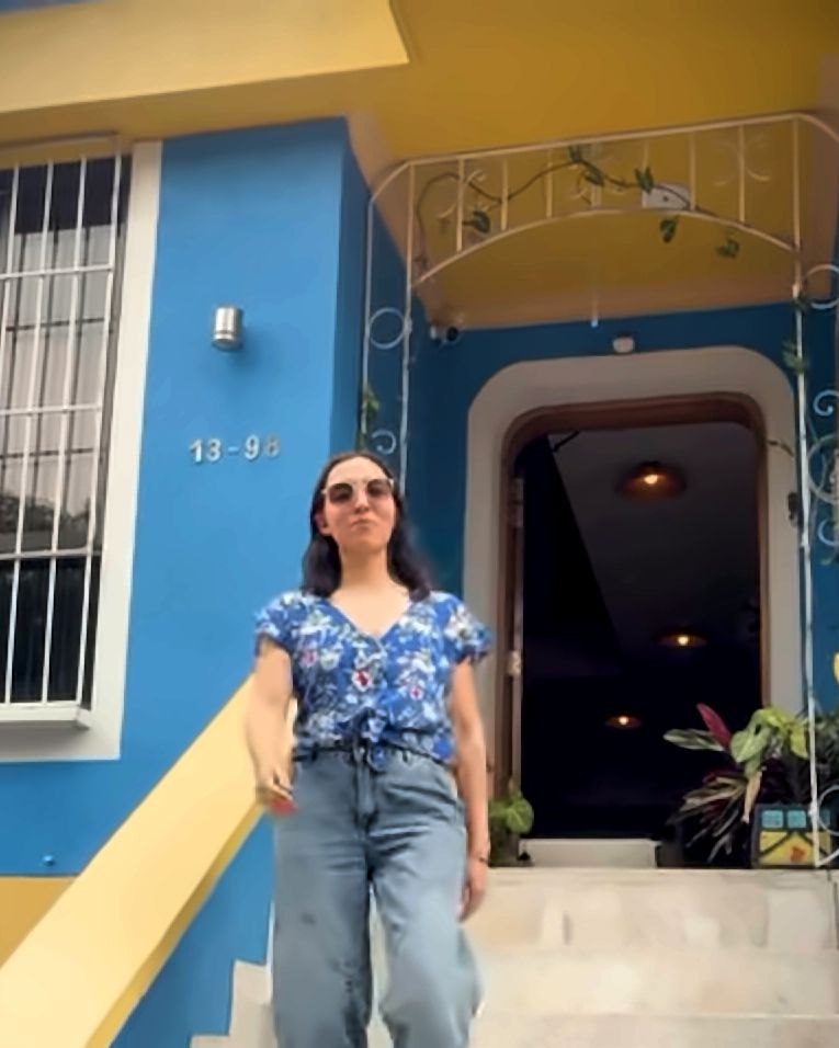 Entrada de Casa Azul: fachada azul con el número 13-98, escalones de piedra y baranda blanca mientras una persona baja la escalera.