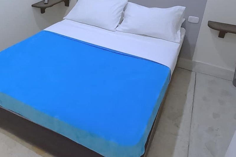 Habitación Caturra: cama doble con cobija azul y repisas a cada lado del cabecero.