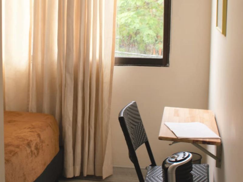 Habitación Maragojipe: cama sencilla, escritorio de madera con silla y ventana con cortinas.