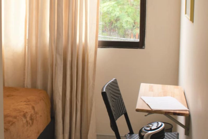 Habitación Maragojipe: cama sencilla, escritorio de madera con silla y ventana con cortinas.